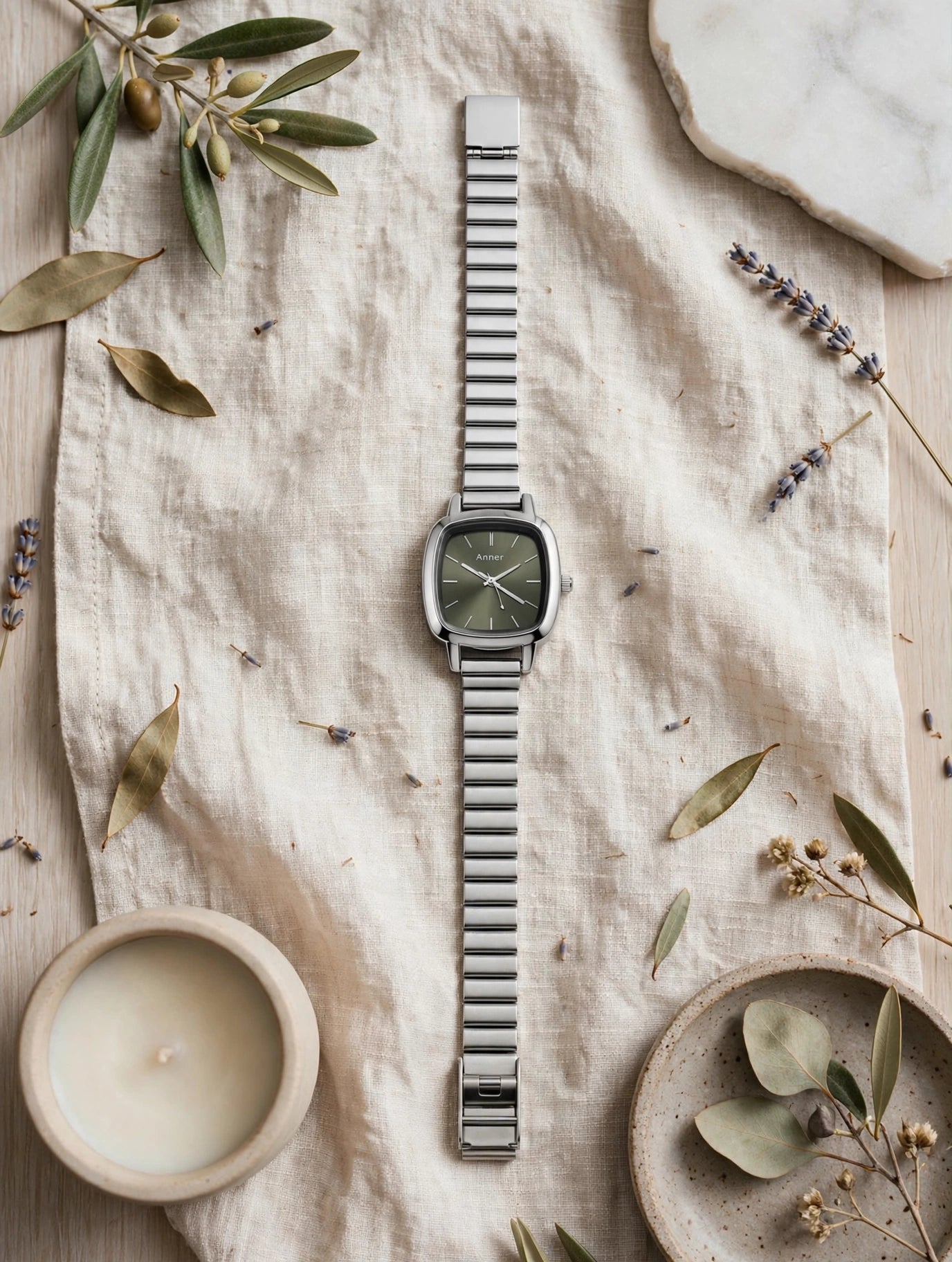 A silver-toned metal watch with a square green dial is laid flat 